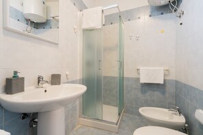 Een badkamer met een douche met glazen wand, twee wasbakken en een spiegel.