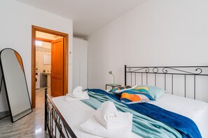 Hotelkamer met een bed, een spiegel, een badkamer zichtbaar door een geopende deur en een tafeltje met een groene plant.
