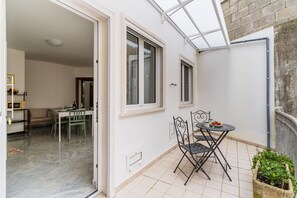Een open woonoppervlak met een eettafel en stoelen, een klein keukenhoekje en een balkon met een bloempot.