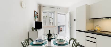 A dining area with a table set for four, a television, and a kitchen area with cabinets and a kettle.