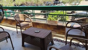 Un balcon agrémenté de meubles en osier, d’une petite table et offrant une vue sur les voitures garées et la verdure.