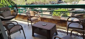 A balcony with wicker furniture, a small table, and a view of parked cars and greenery. - Spacious 3-bedroom Apartment in Central Cairo With City View (Cairo)