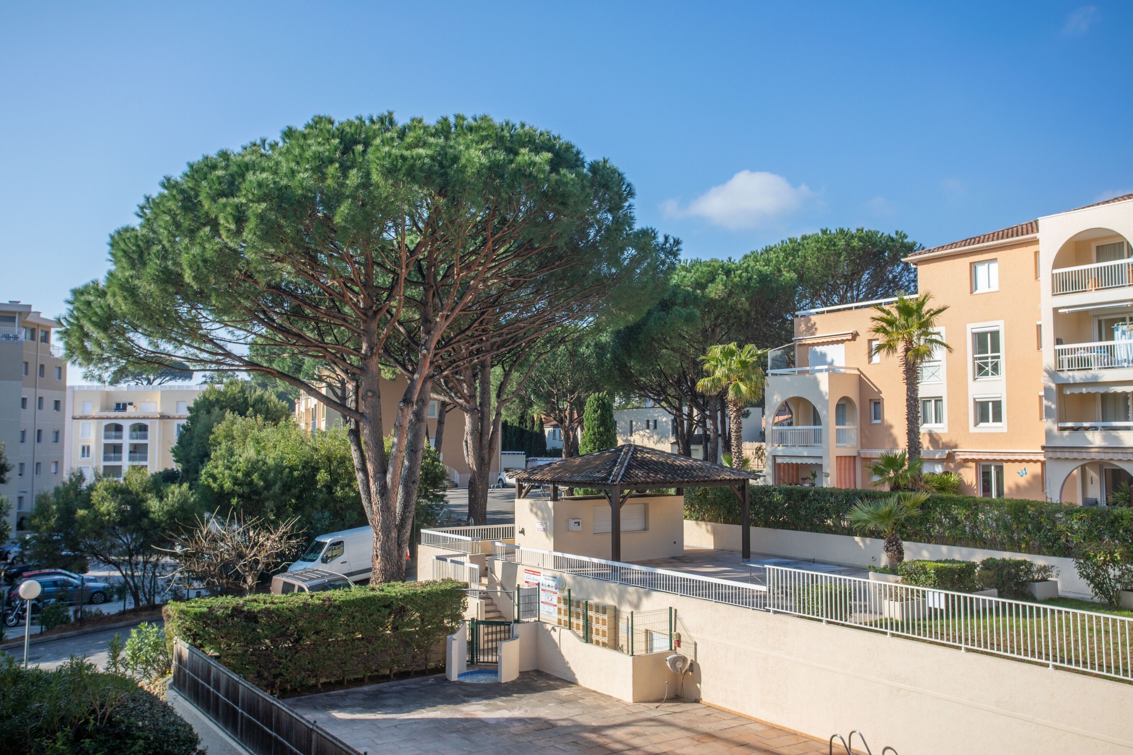 A residential area with a large tree, a covered seating area, and a building with balconies.