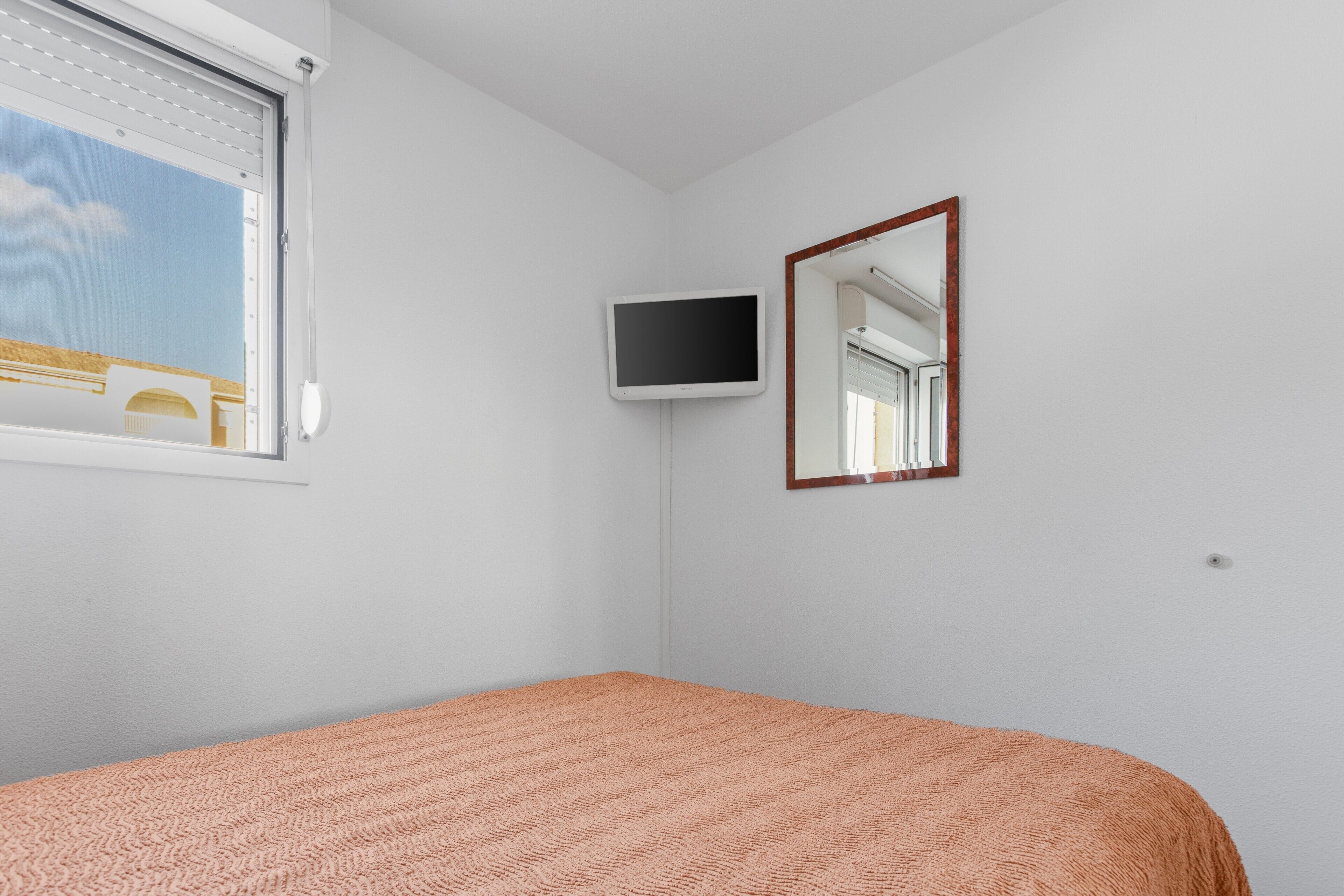 A bedroom with a bed, a television, a mirror, and a window with blinds.