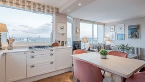 A modern kitchen with white cabinetry, a dining table with pink chairs, and a view of the city through large windows. - AVAL Lovely 2-bed flat with balcony in Notting Hill, West London (London)