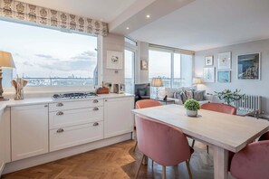A modern kitchen with white cabinetry, a dining table with pink chairs, and a view of the city through large windows. - AVAL Lovely 2-bed flat with balcony in Notting Hill, West London (London)
