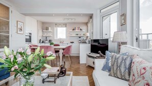 A modern living room with a sofa, a coffee table, and a TV. There is a dining area with a table and chairs. The room has a large window and a kitchen in the background. - AVAL Lovely 2-bed flat with balcony in Notting Hill, West London (London)