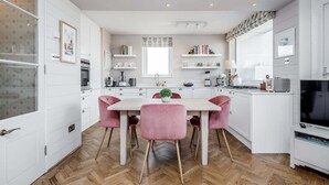 A modern kitchen with white cabinetry, a central island, pink chairs, and a television on the right. - AVAL Lovely 2-bed flat with balcony in Notting Hill, West London (London)