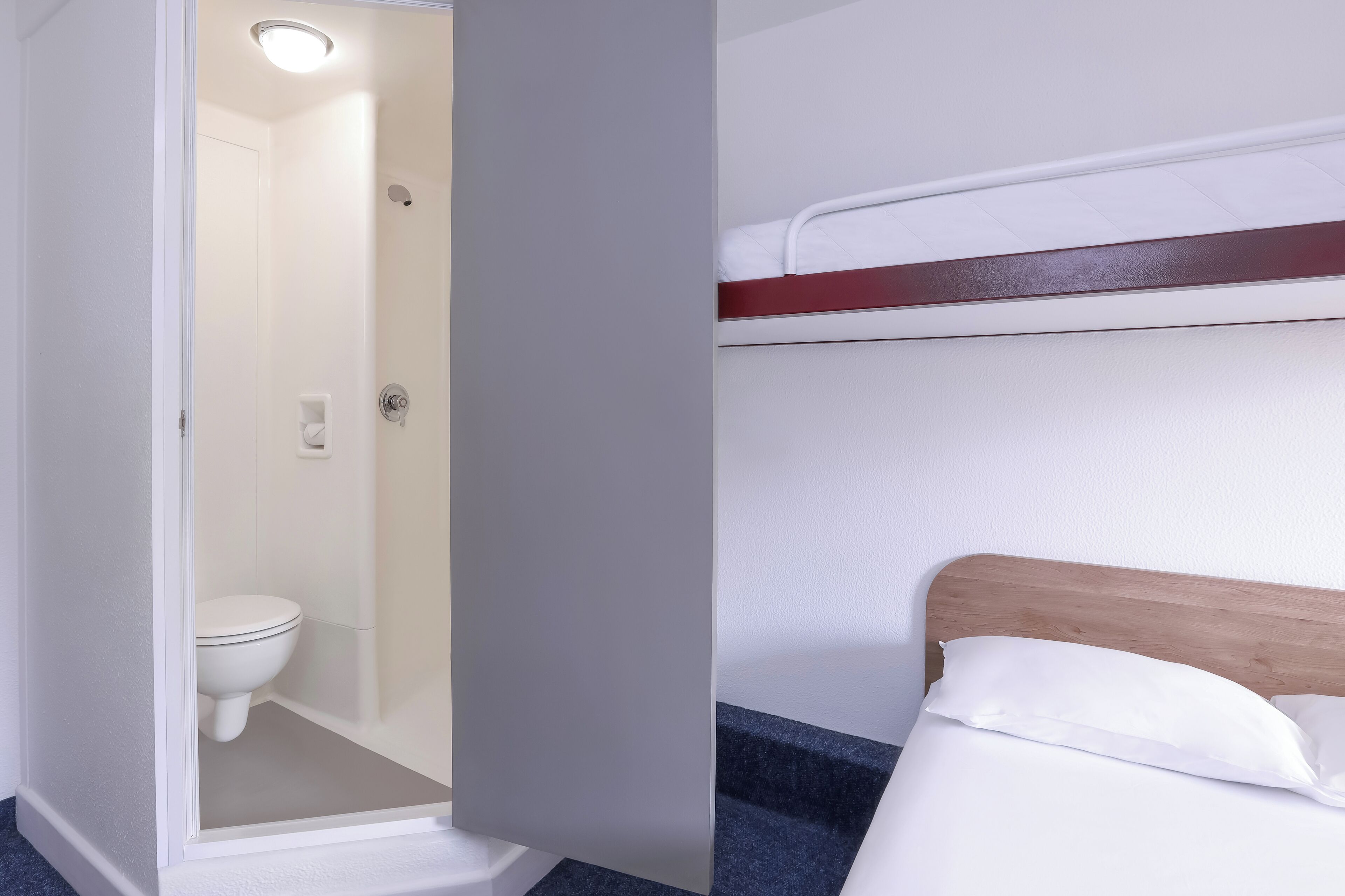 A bathroom with a toilet and shower, and a bed with a wooden headboard and white bedding.