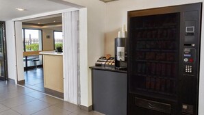A hotel reception area with a vending machine, a counter, and a seating area with a bench and a table. - SUN1 Parow Cape Town (Cape Town)