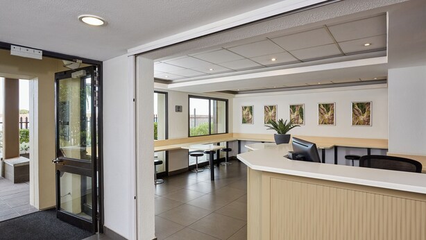 A modern reception area with a glass door entrance, a counter, and several tables and chairs. - SUN1 Parow Cape Town (Cape Town)
