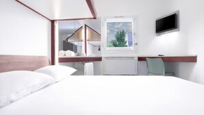 A hotel room with a large bed, a desk with a chair, a TV mounted on the wall, and a window with a view of buildings and trees. - SUN1 Parow Cape Town (Cape Town)