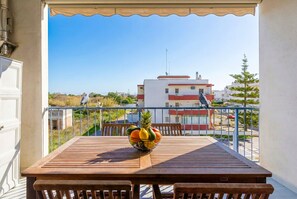 A balcony with a table and chairs, a fruit bowl, and a view of buildings and greenery. - Circe Sea View Apartment Otranto – Charming Studio with Terrace, Wi-Fi & AC (Otranto)