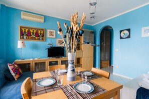 A dining area with a table set for four, a vase with dried plants, and a television in the background. - Circe Sea View Apartment Otranto – Charming Studio with Terrace, Wi-Fi & AC (Otranto)