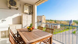 A balcony with a wooden table, chairs, a fruit bowl, and a view of the cityscape. - Circe Sea View Apartment Otranto – Charming Studio with Terrace, Wi-Fi & AC (Otranto)