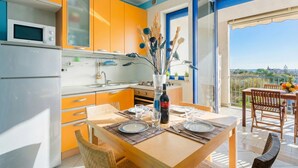 A modern kitchen with a dining area, a balcony with a view, and a table set for two. - Circe Sea View Apartment Otranto – Charming Studio with Terrace, Wi-Fi & AC (Otranto)