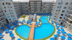 Um hotel moderno com piscina central, várias varandas e espreguiçadeiras.