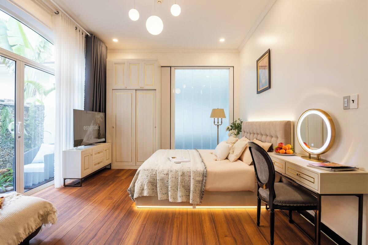 A bedroom with a bed, bedside table, chair, TV, and a large window with curtains.