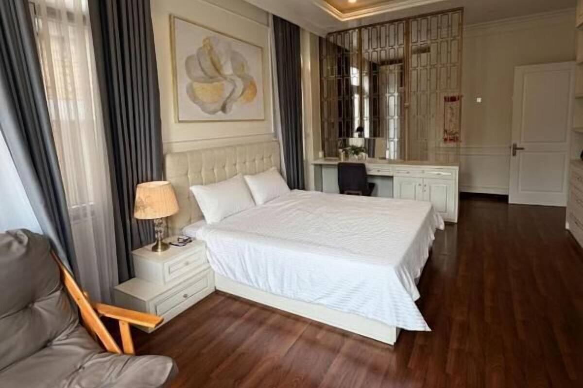 A hotel room with a large bed, a desk, a chair, and a wardrobe.