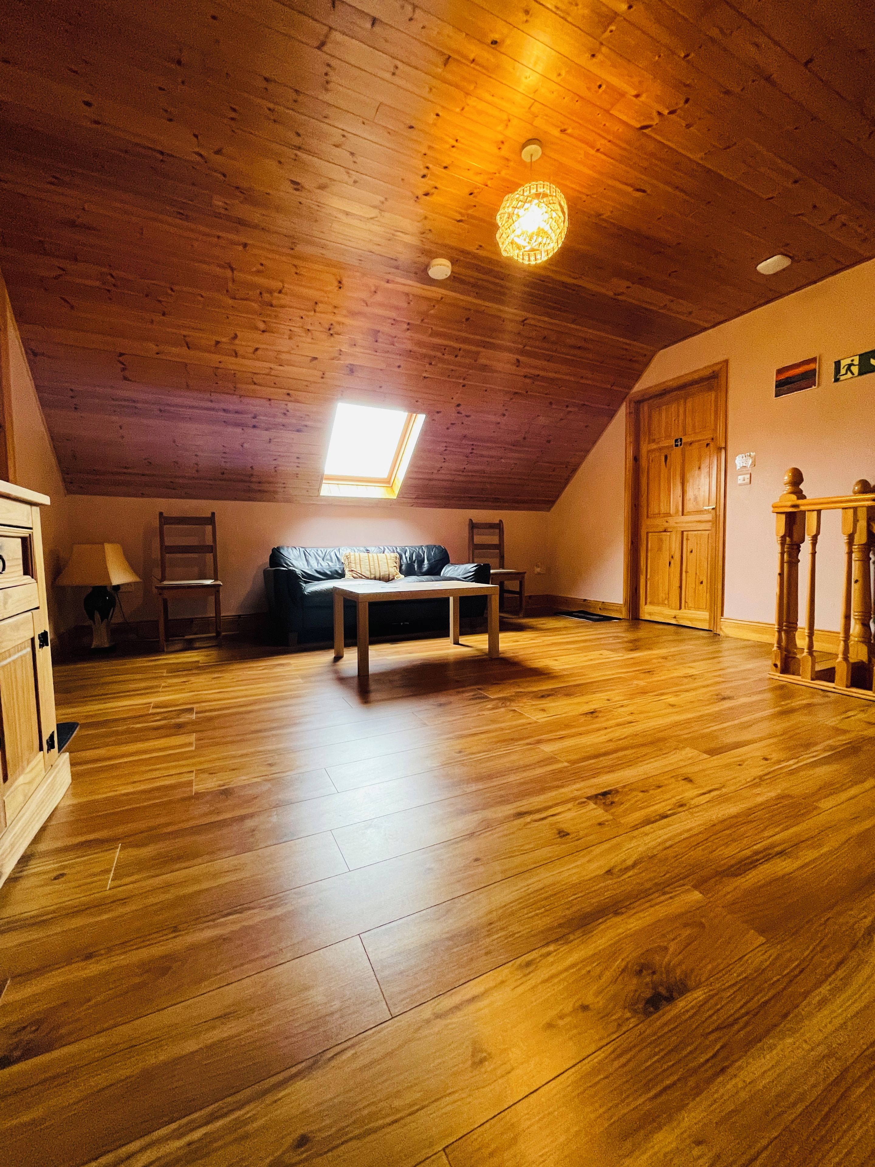 A room with wooden flooring, a sofa, a table, and a skylight.