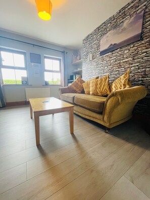 A living room with a sofa, a coffee table, and a stone wall. - Tinnies Guest House (Valentia Island)