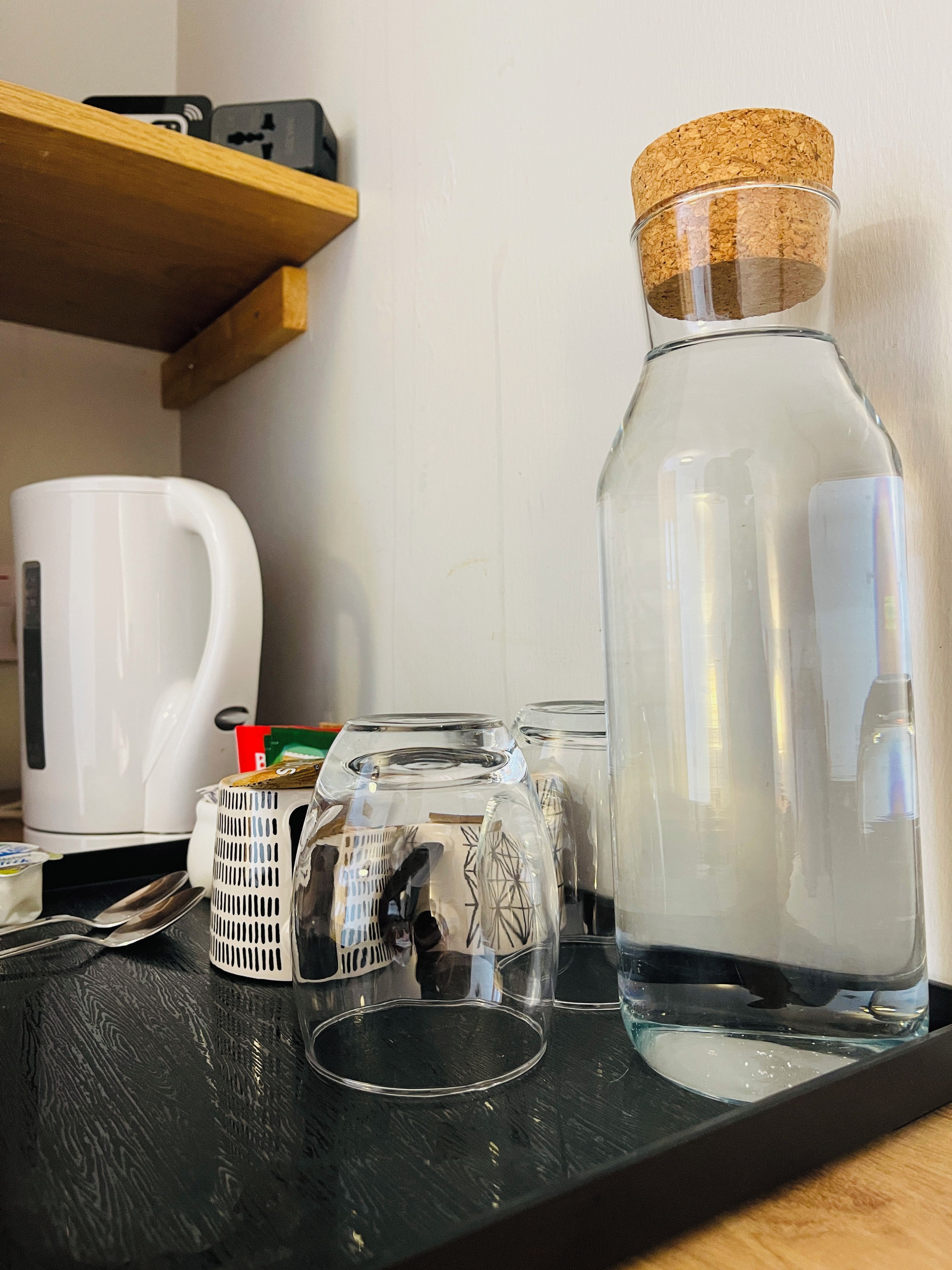 Una encimera de cocina con una cafetera, una botella de vidrio con tapón de corcho y un juego de vasos de cristal.