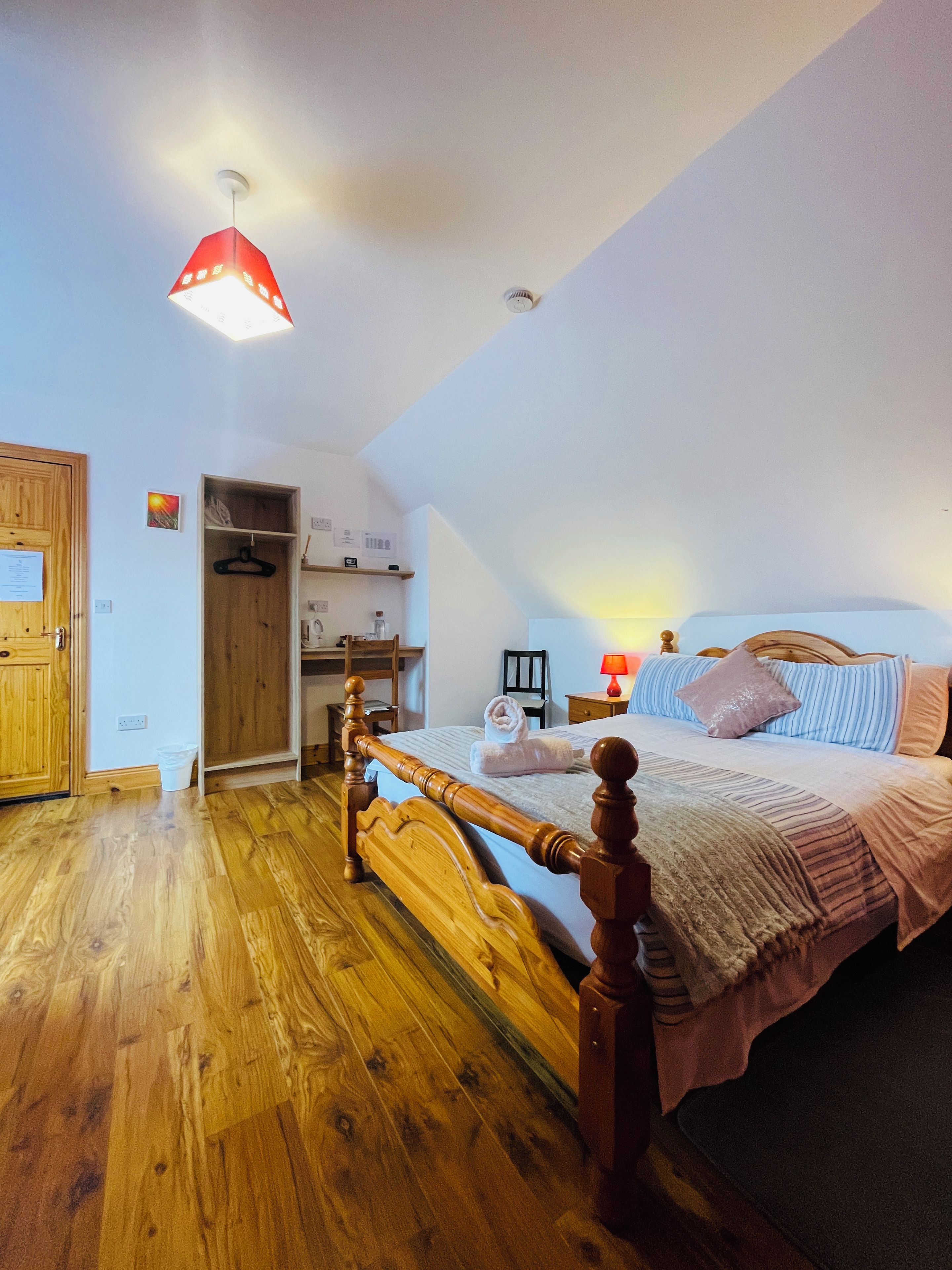 A bedroom with a wooden bed, a hanging light fixture, a bedside table, and a wardrobe.