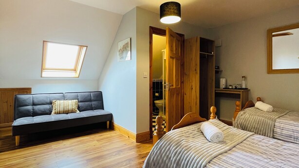 A bedroom with a sofa, two beds, a wooden ceiling, and a skylight. - Tinnies Guest House (Valentia Island)