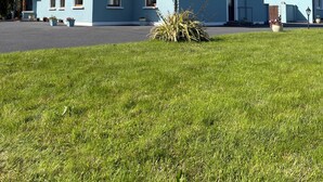 A light blue house with a grey roof, a front porch, and a small garden. - Tinnies Guest House (Valentia Island)