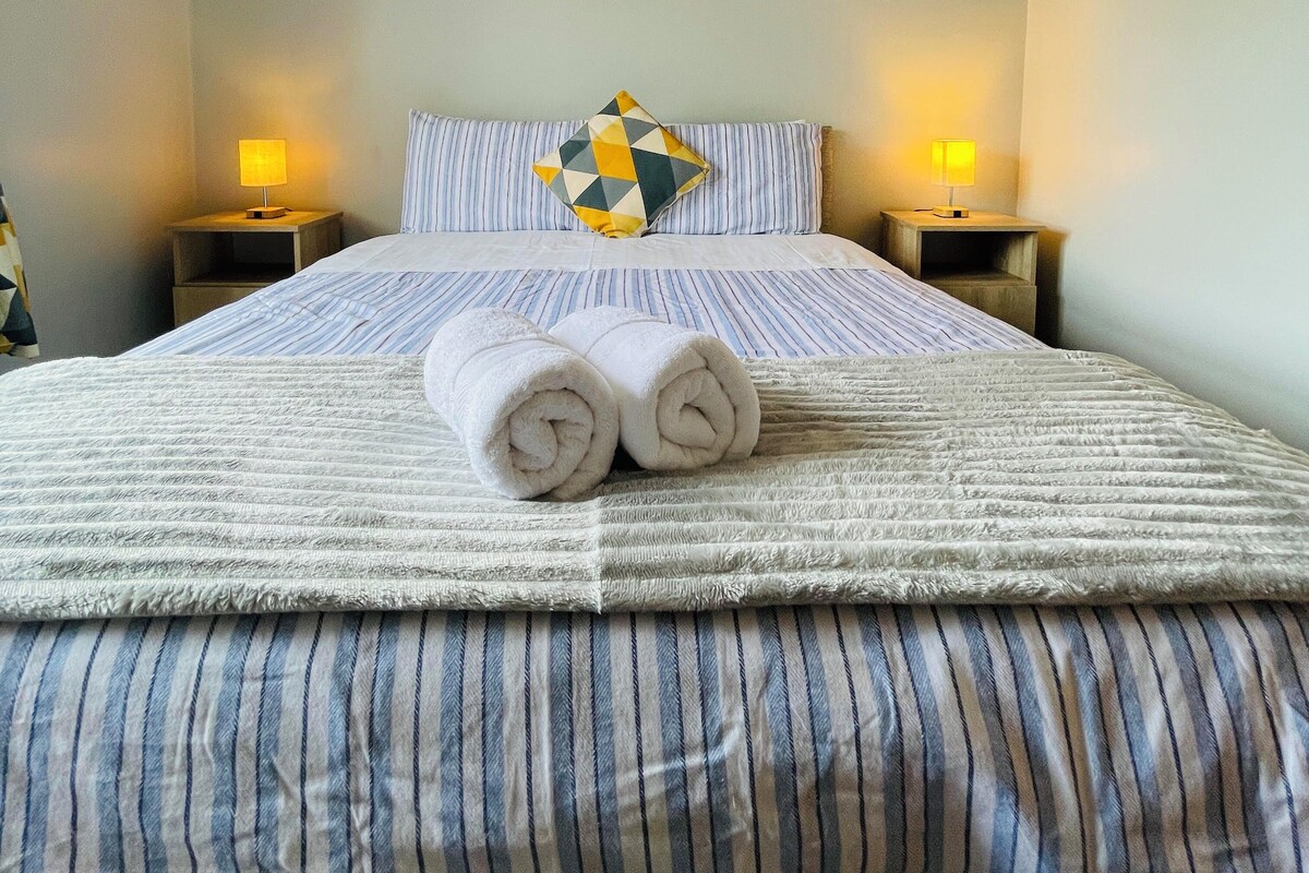 A neatly made bed with striped bedding, a pillow with a geometric pattern, and a red rose painting on the wall.