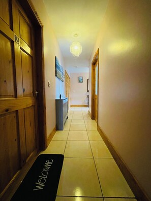 A hotel hallway with a welcome mat, wooden doors, a radiator, and a chandelier.