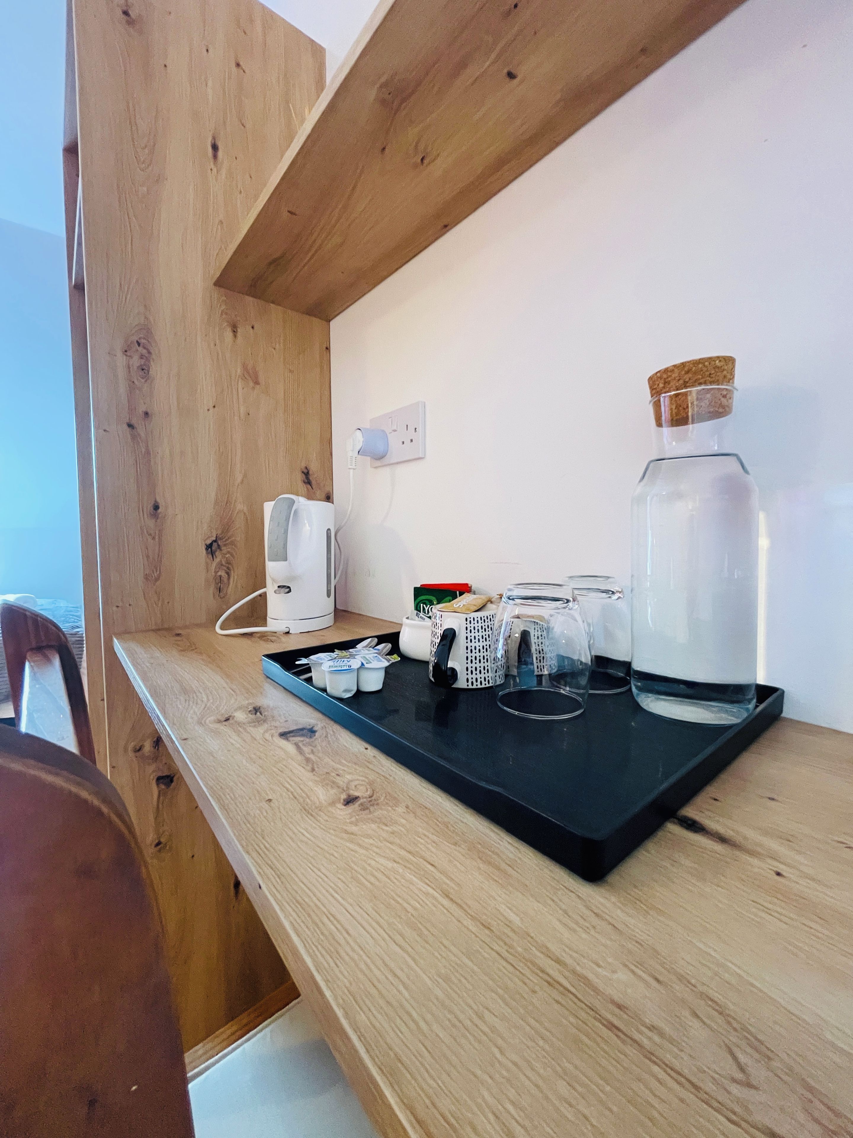 A kitchen counter with a coffee maker, a kettle, a glass jar, and a tray with utensils.