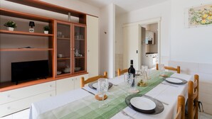 Een eethoek met een tafel voor vier personen, een televisie op een kast en een keuken op de achtergrond.