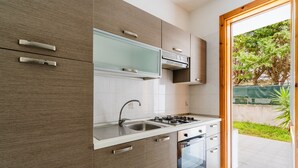 Een moderne keuken met een gasfornuis, spoelbak en oven, houten keukenkastjes en uitzicht op groen.