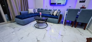 Ein modernes Wohnzimmer mit einem blauen Sofa, einem Glastisch und einem Essbereich mit Stühlen.