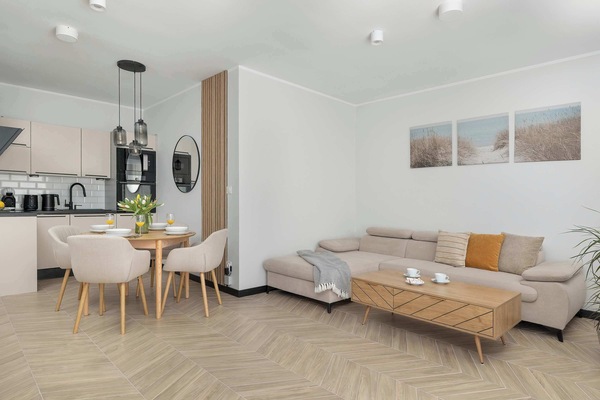 A bright open-space area featuring a comfortable beige sofa, a coffee table, and a dining area with a round table and four chairs.