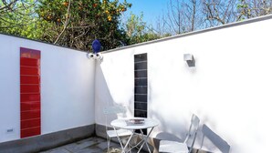 A small outdoor patio with a white table and two chairs, a red door, and a black window. - Domus Pio XI (Sant'Agnello)