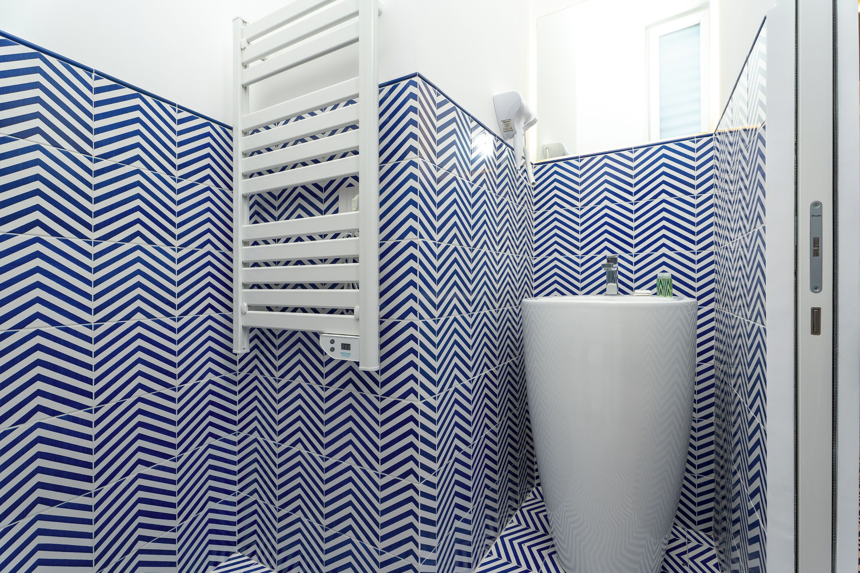 Un baño con pared de azulejos estampados en patrón chevron, un lavamanos blanco y un perchero.