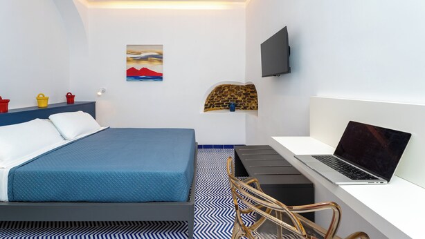 A modern hotel room with a bed, a desk with a laptop, a TV, and a painting on the wall. - Domus Pio XI (Sant'Agnello)