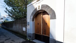 A building with a wooden door under a stone archway, a plaque above the door, and a stone wall to the left. - Domus Pio XI (Sant'Agnello)