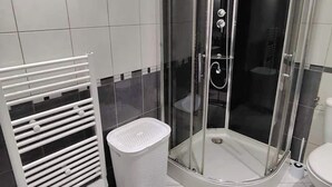 A modern bathroom with a glass-enclosed shower, a white radiator, and a white laundry basket. - Large 47 m² renovated family apartment on 1st floor - Portes des Ardennes (Charleville-Mézières)