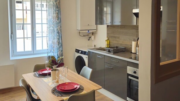 A compact kitchen with modern appliances, a dining area with a table and chairs, and a window with curtains. - Large 47 m² renovated family apartment on 1st floor - Portes des Ardennes (Charleville-Mézières)