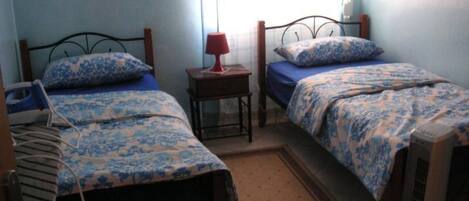 A bedroom with two beds, a bedside table with a lamp, and an air conditioning unit.