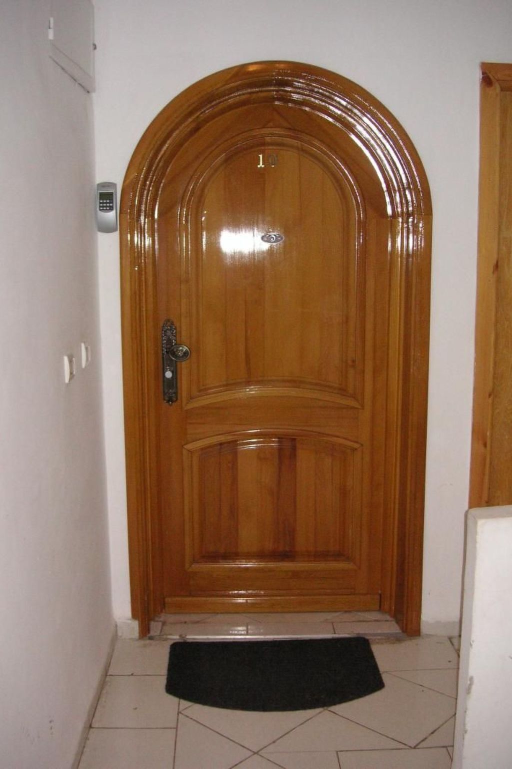 A wooden door with a keypad lock, a small mat at the entrance, and a light switch on the wall to the left.