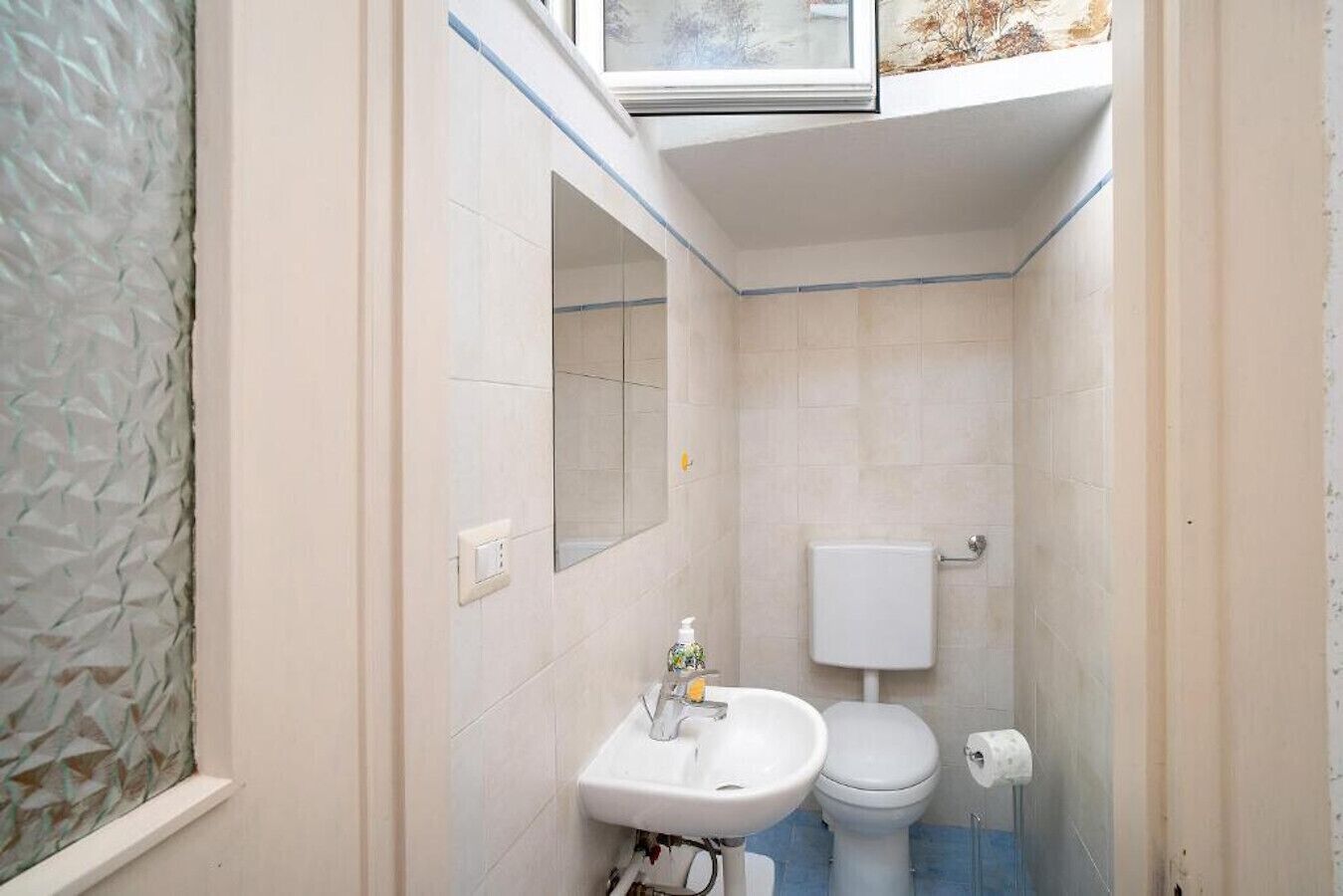 Ein kleines, kompaktes Badezimmer mit Toilette, Waschbecken und einem Fenster über dem Waschbecken.