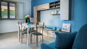 Un área de comedor moderna con una mesa, sillas, un jarrón de flores y una estantería con objetos decorativos.