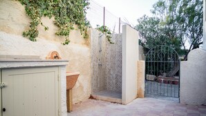 Un baño exterior pequeño con lavamanos, ducha y portón.