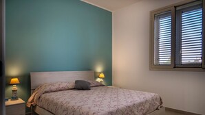 Un dormitorio con una cama, dos lámparas de noche, una ventana con persianas y paredes color turquesa.