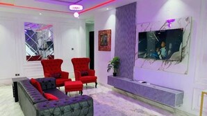 Una sala de estar moderna con un sofá gris, sillones rojos y un televisor grande montado en la pared.