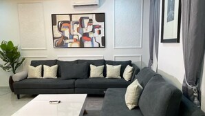 A modern living room with a dark grey sectional sofa, a white coffee table, and a large abstract painting on the wall. - Stylish 2-Bed Luxury Apartment in Ikeja GRA – 24/7 Power & Comfort (Lagos)